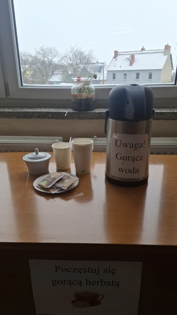 Dzbanek, cukiernica, herbata oraz kubki jednorazowe na tle zimowego okna.